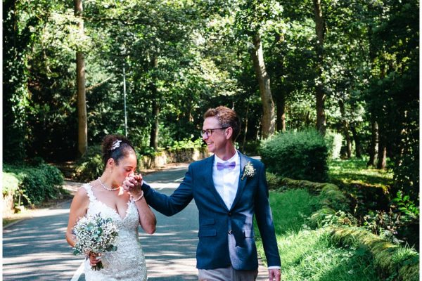 bride kisses the grooms hand whilst walking through the woods