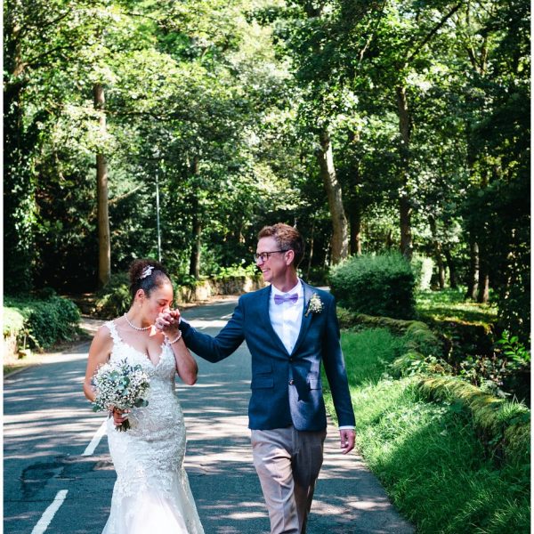 bride kisses the grooms hand whilst walking through the woods