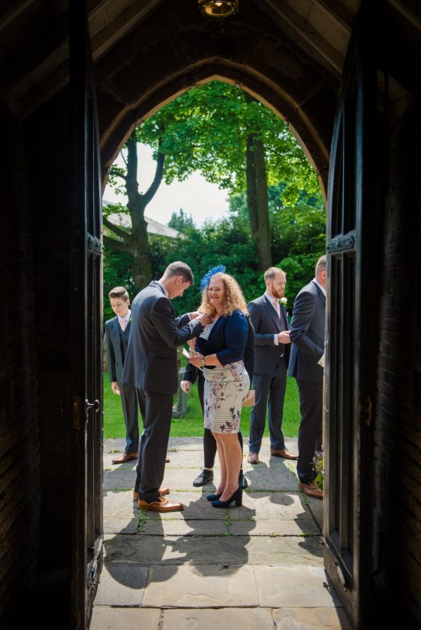 groom helps guests in doorway of church