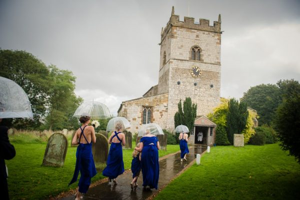 Wedding party and bride enter church via path on rainy day