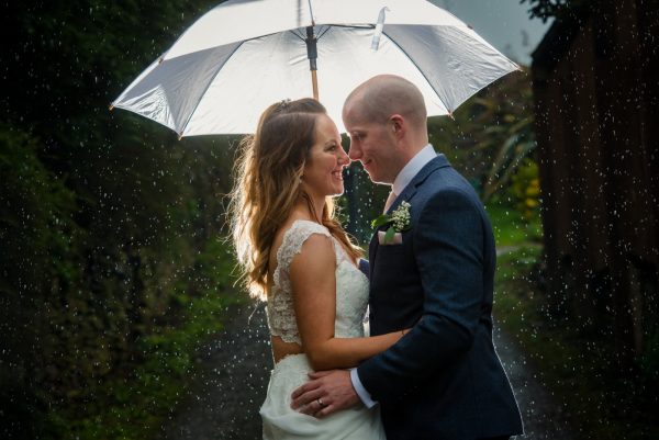 Umbrella in the rain with bride and groom