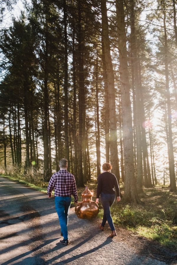 couple walking with gin still through beautiful trees in sunlight