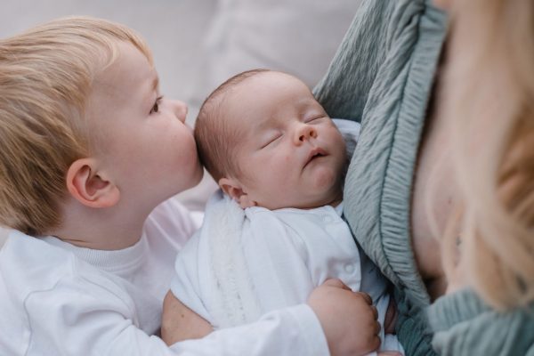 newborn baby being held by mother and being cuddled by his brother colour image