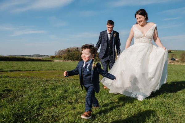 bride and groom run after little boy in a suit little suit