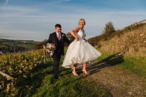 Brides lifts her dress out of the muddy path as she walks with her new husband