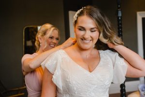 bride and her sister putting the final touches to her outfit before the ceremony. Bride lifts hair so sister can fasten her necklace.
