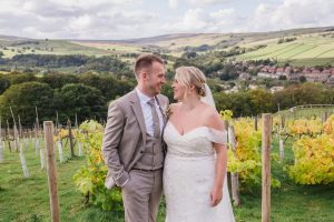 the newlywed bride and groom look at each other with rolling hills and vines growing in the background at Holmfirth Vineyard